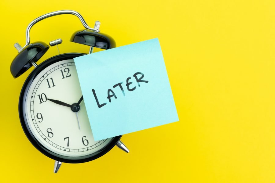 Sticky post with handwriting the word Later stick on alarm clock on solid yellow background with copy space using as procrastination, self discipline or laziness concept procrastination